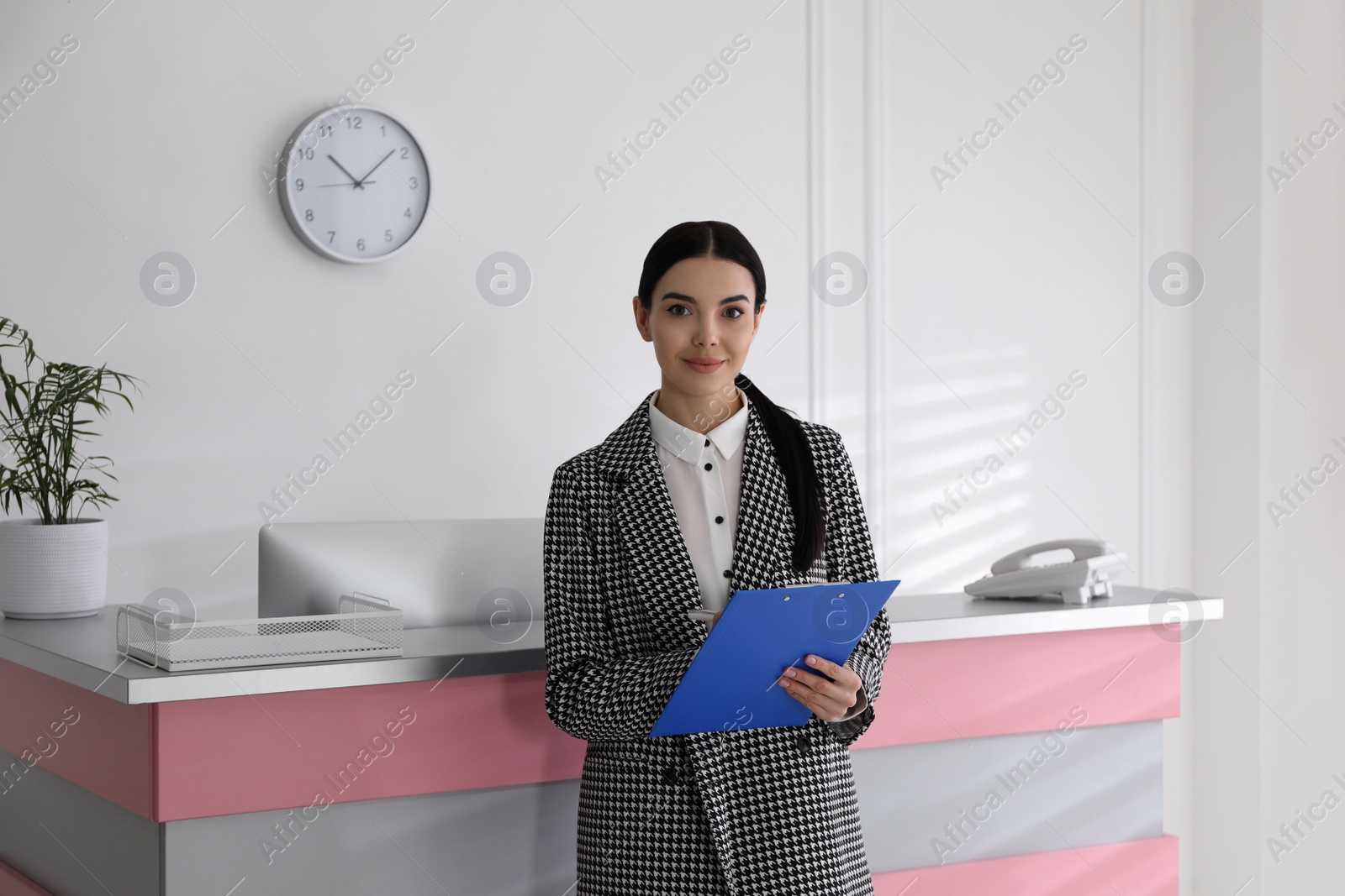 Photo of Receptionist with clipboard near countertop in office