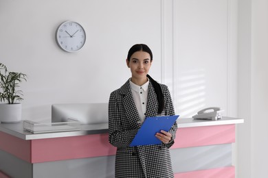 Photo of Receptionist with clipboard near countertop in office