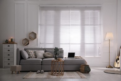 Living room with comfortable grey sofa and stylish interior elements near window