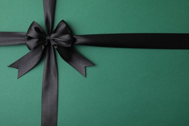 Photo of Black satin ribbon with bow on green background, top view