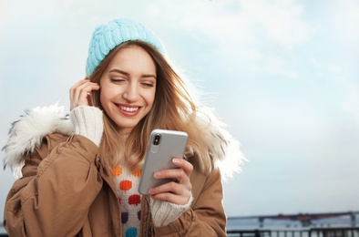 Photo of Young woman using mobile phone outdoors. Space for text