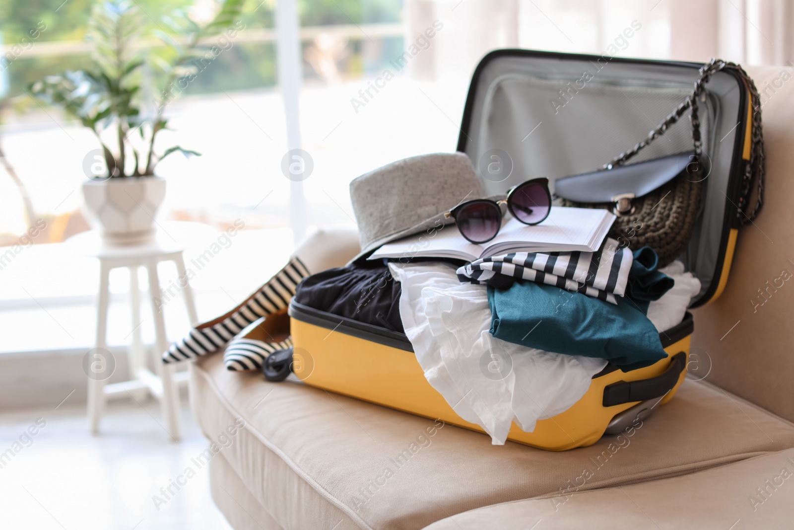 Photo of Open yellow suitcase with different clothes packed for journey at home