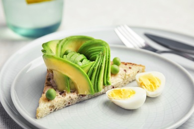 Crisp toast with sliced avocado and quail egg on plate, closeup