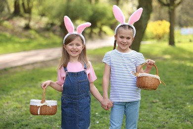 Photo of Easter celebration. Cute little girls with bunny ears holding wicker baskets outdoors