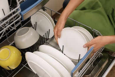 Photo of Young woman loading dishwasher in kitchen, closeup. Cleaning chores