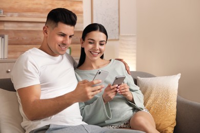 Happy couple in pyjamas with gadgets spending time together on sofa at home