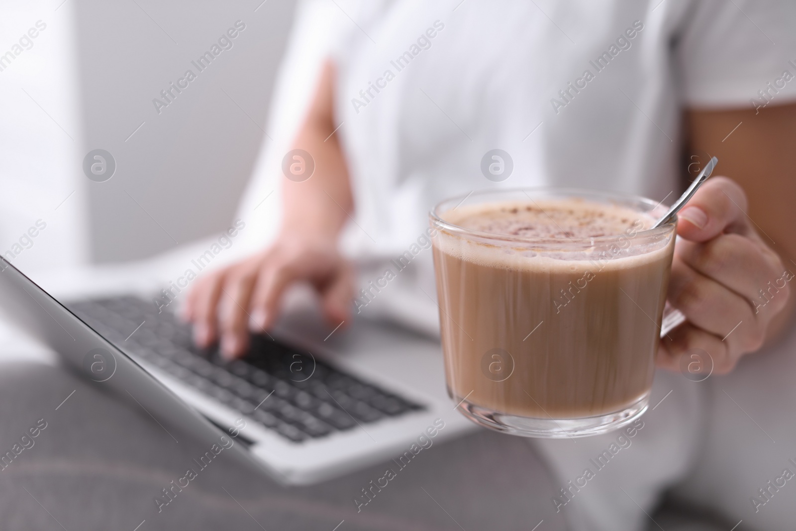 Photo of Woman with cup of morning coffee working on laptop indoors, closeup