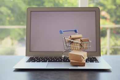 Internet shopping. Laptop and small cart with boxes on table indoors