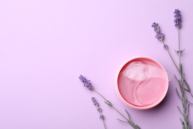 Photo of Under eye patches in jar with spatula and lavender flowers on lilac background, flat lay. Space for text