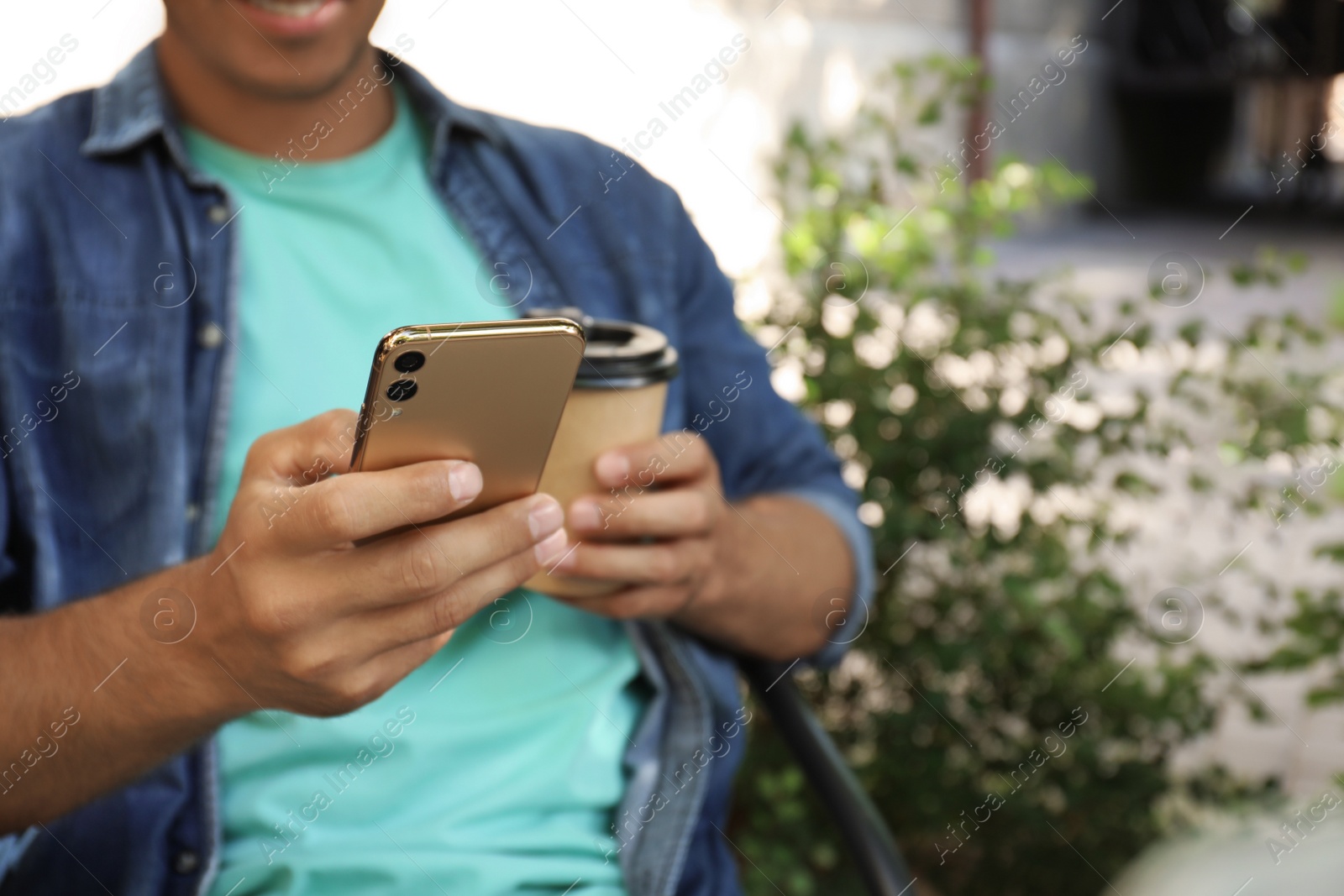 Photo of Man with smartphone and cup of coffee outdoors, closeup