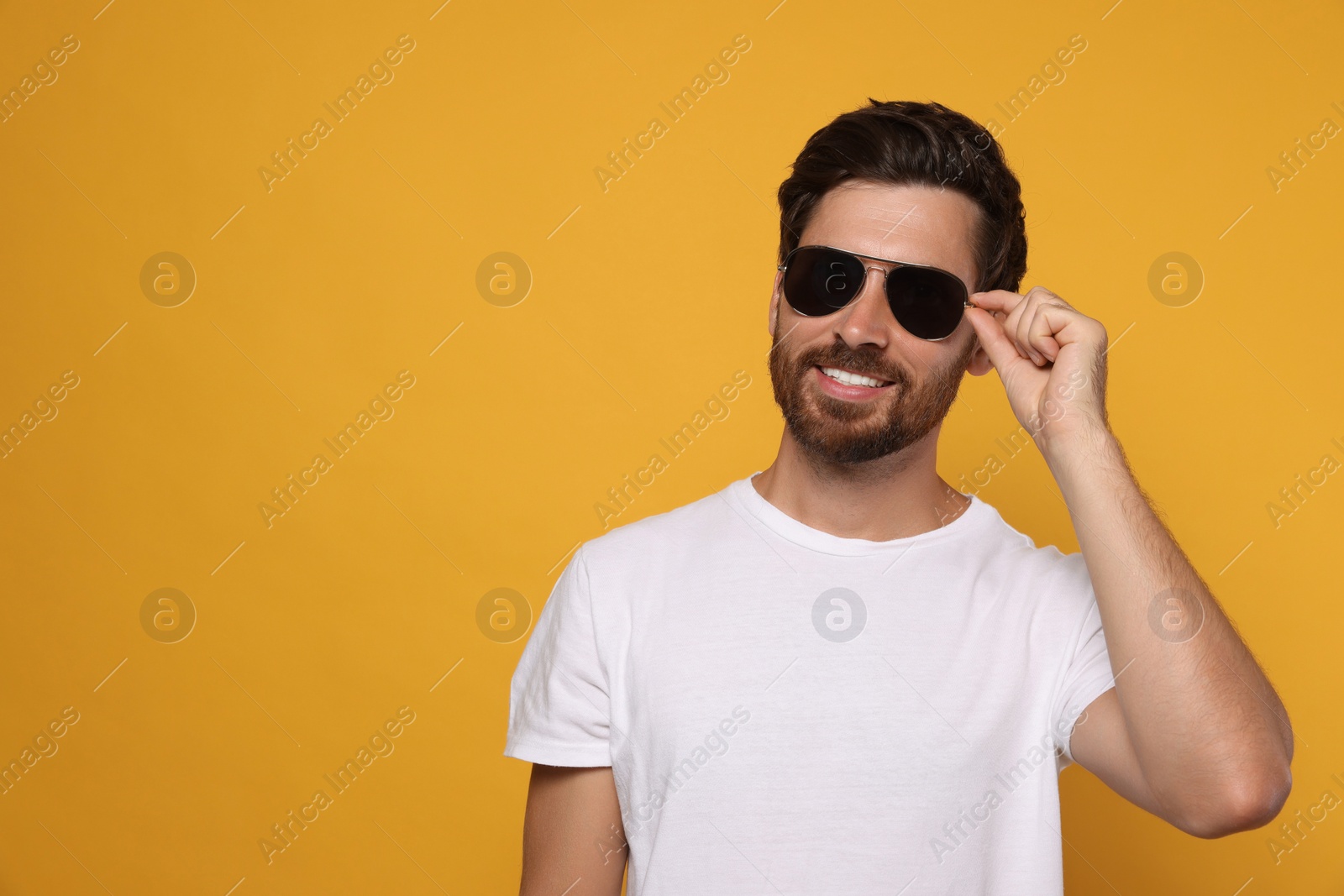 Photo of Portrait of smiling bearded man with stylish sunglasses on orange background. Space for text