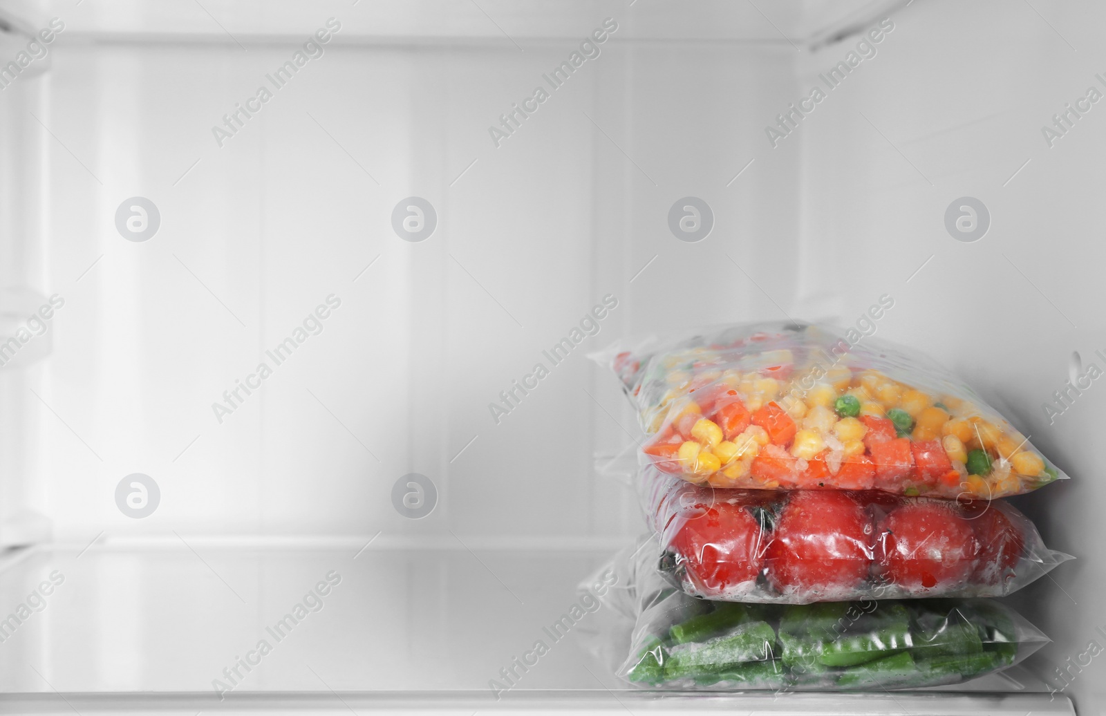 Photo of Plastic bags with different frozen vegetables in refrigerator. Space for text