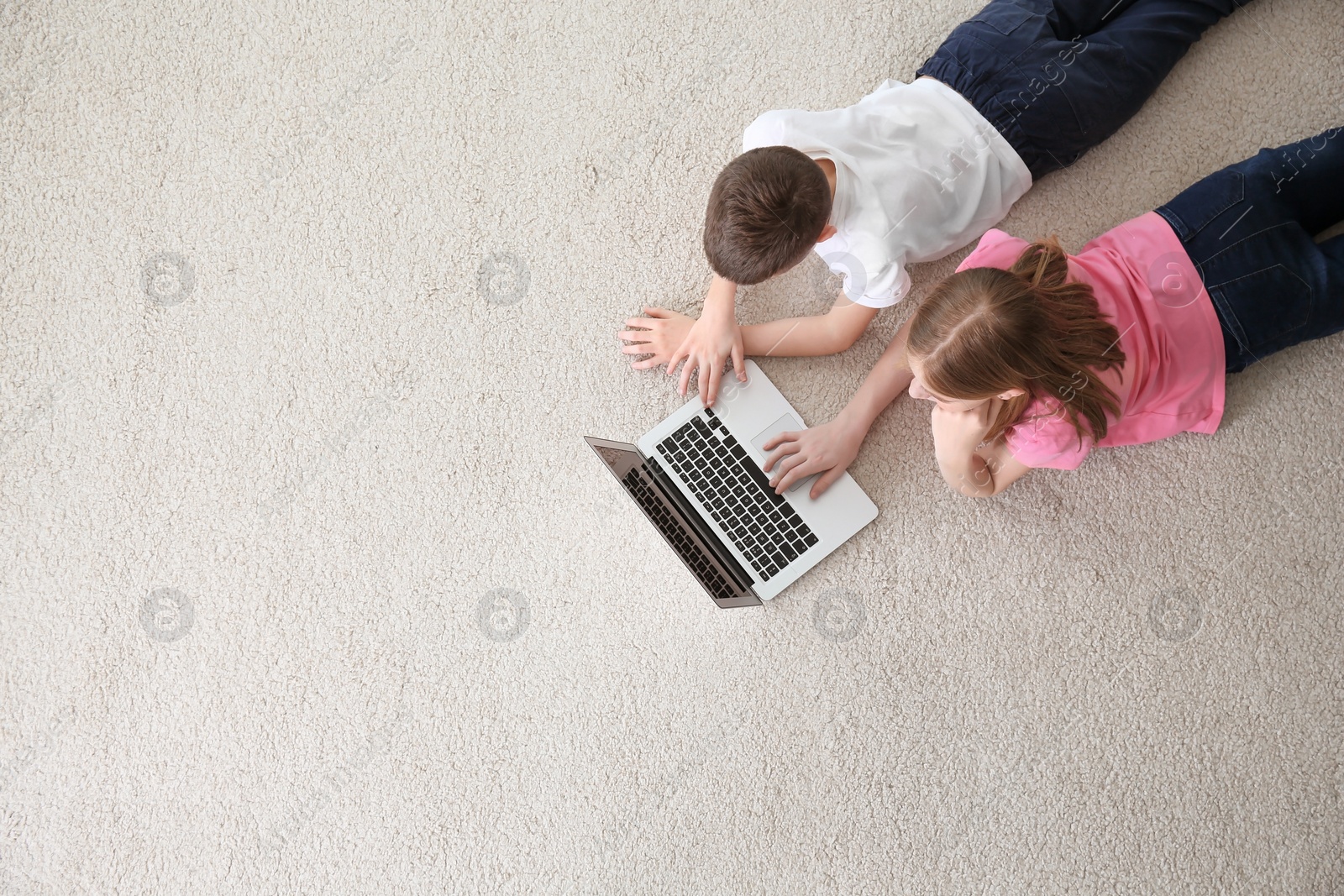 Photo of Teenage girl and her brother with laptop lying on cozy carpet at home