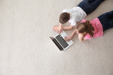 Teenage girl and her brother with laptop lying on cozy carpet at home