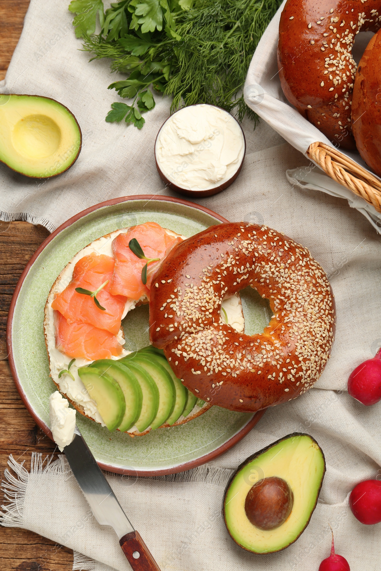 Photo of Delicious bagel with cream cheese, salmon and avocado on table, flat lay