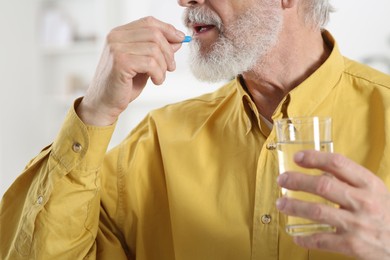 Photo of Senior man with glass of water taking pill indoors, closeup