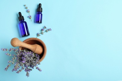 Bottles of essential oil, mortar and pestle with lavender flowers on light blue background, flat lay. Space for text