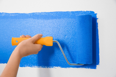 Photo of Woman painting white wall with blue dye, closeup. Interior renovation