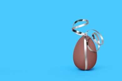 Photo of Delicious chocolate egg with silver ribbon on light blue background. Space for text