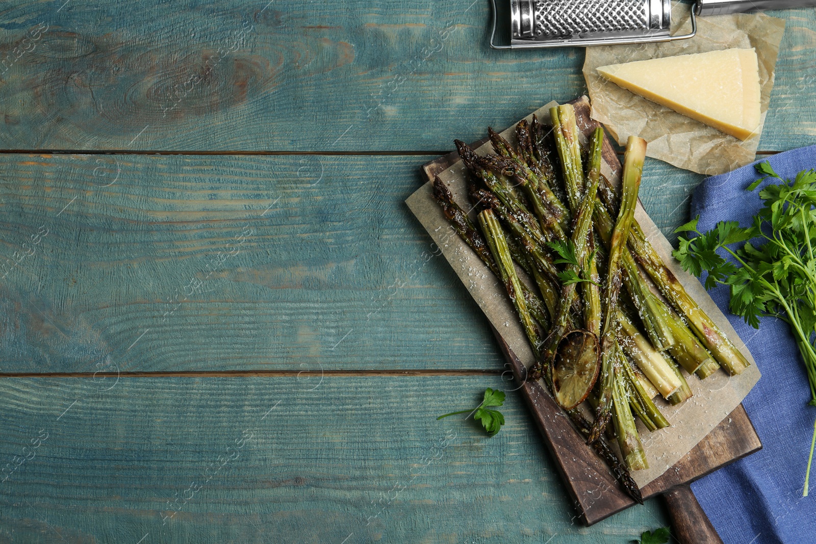 Photo of Oven baked asparagus served with lemon and parsley on blue wooden table, flat lay. Space for text