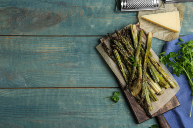 Oven baked asparagus served with lemon and parsley on blue wooden table, flat lay. Space for text