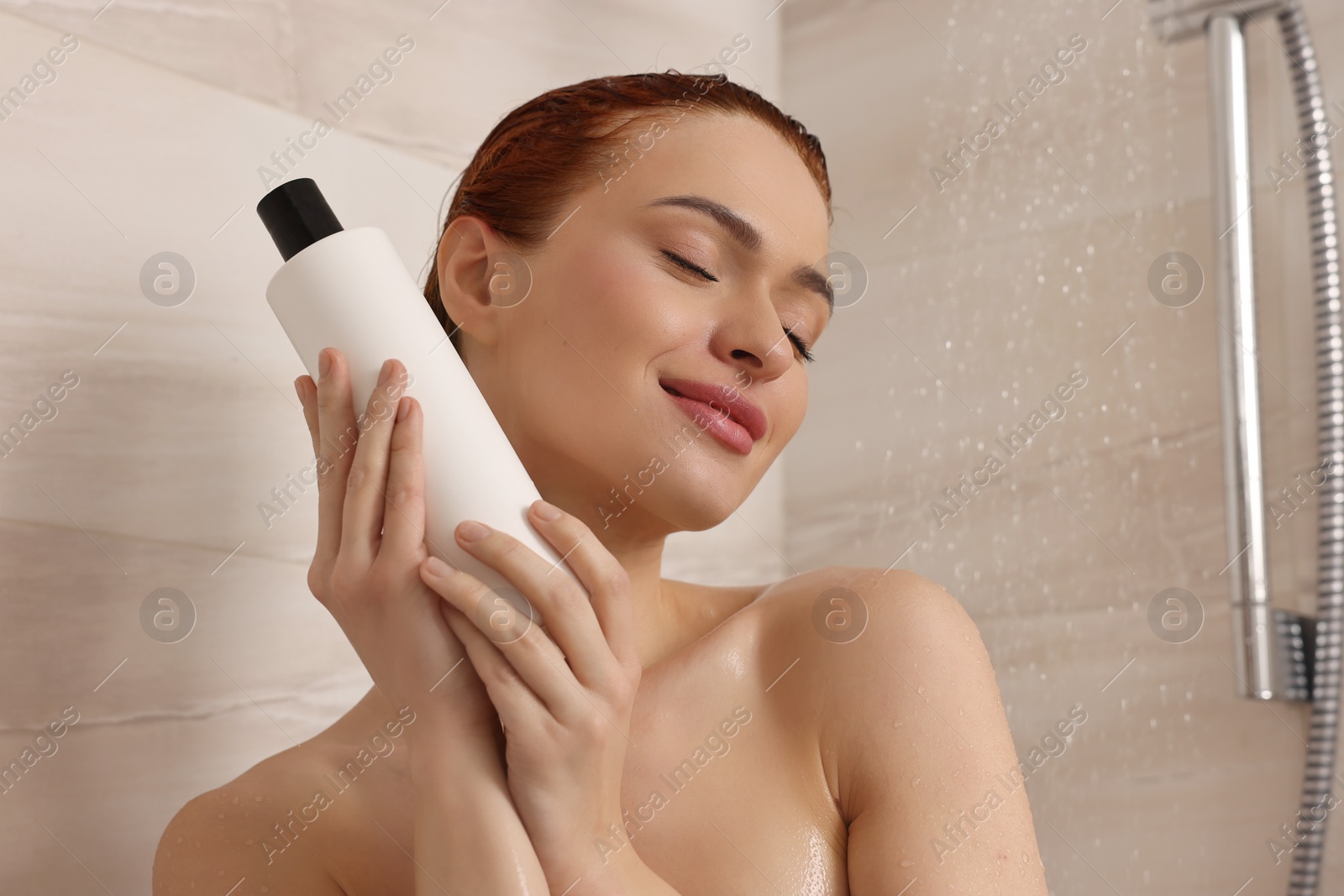 Photo of Happy young woman with bottle of shampoo in shower