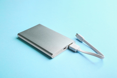 Photo of Modern portable charger with cable on light blue background