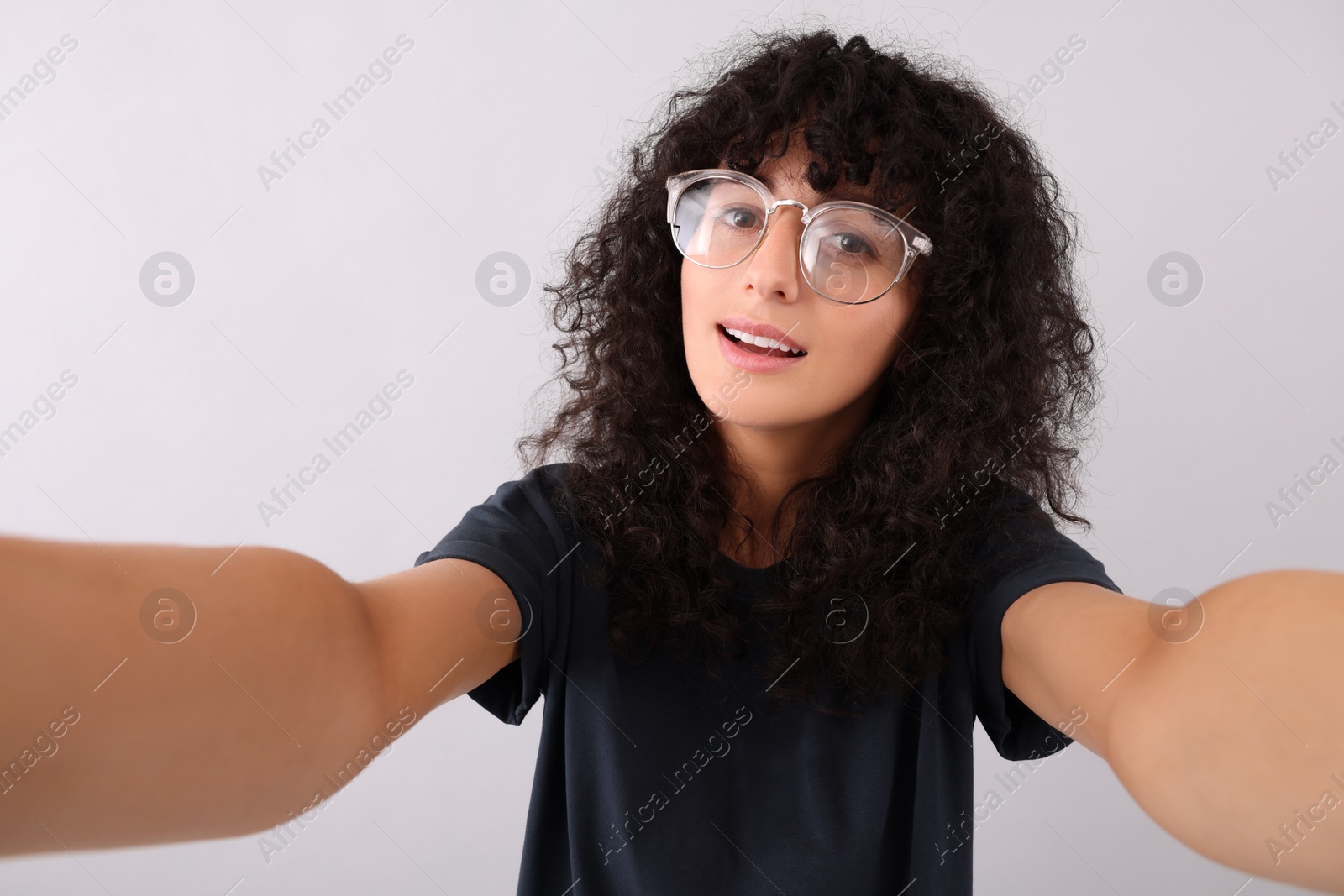 Photo of Beautiful young woman in eyeglasses taking selfie on light grey background