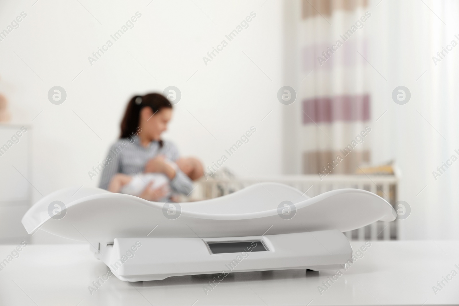 Photo of Modern baby scales on table and blurred woman with child indoors. Space for text