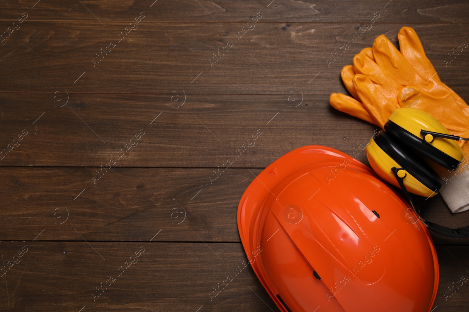 Photo of Hard hat, earmuffs and gloves on wooden table, flat lay with space for text. Safety equipment