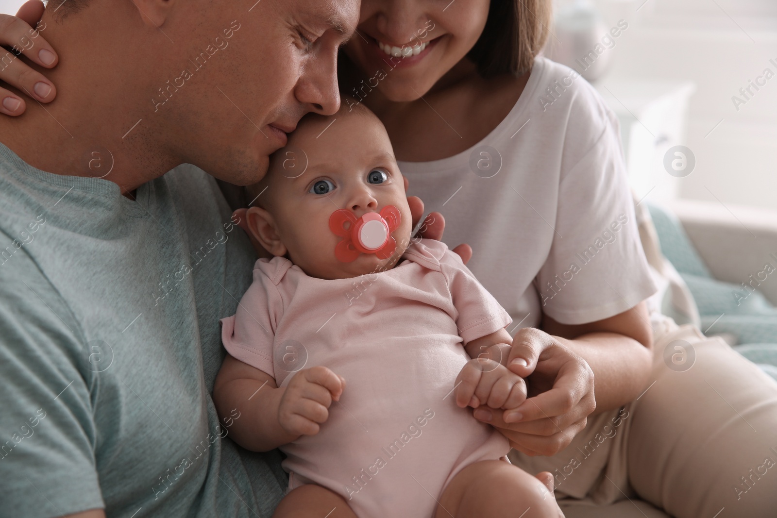 Photo of Happy couple holding their cute little baby with pacifier indoors