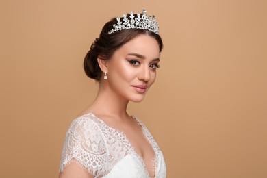 Beautiful young woman wearing luxurious tiara on beige background