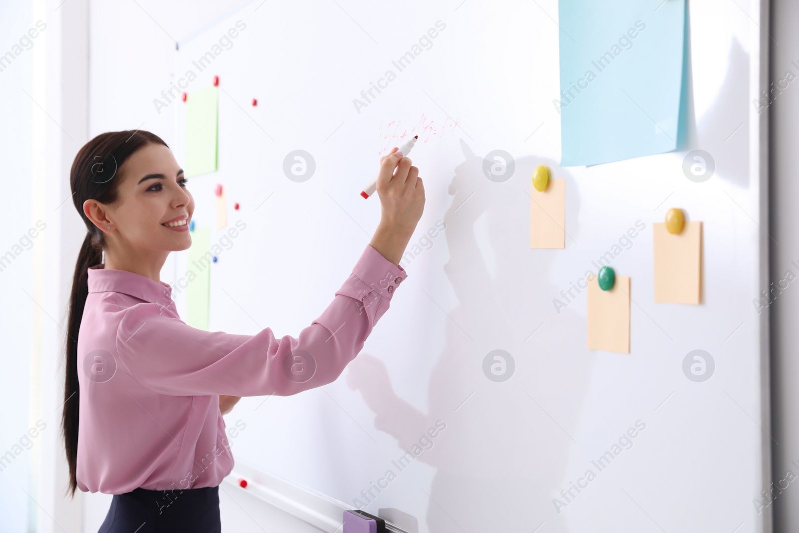 Photo of Young teacher writing on whiteboard in classroom