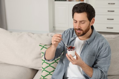 Handsome man with delicious yogurt on sofa at home. Space for text