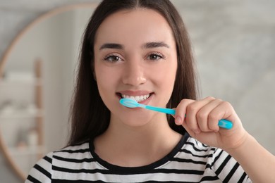 Young woman brushing her teeth with plastic toothbrush in bathroom