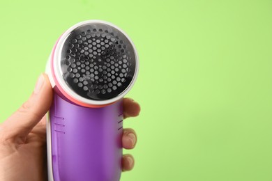Photo of Woman holding modern fabric shaver on light green background, closeup. Space for text