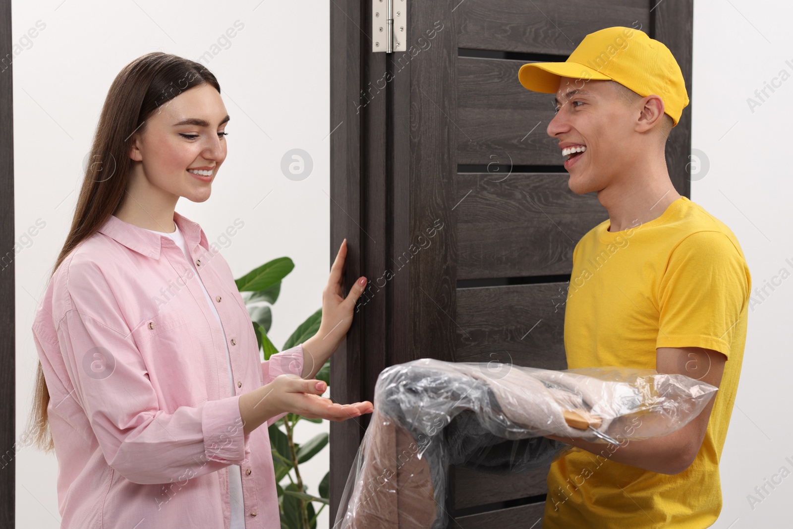 Photo of Dry-cleaning delivery. Courier giving coat in plastic bag to woman indoors