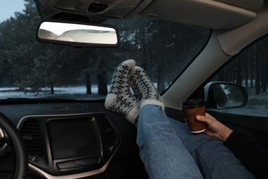 Photo of Young man in warm socks with coffee resting inside car, closeup