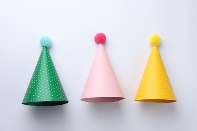 Colorful party hats with pompoms on light background, top view