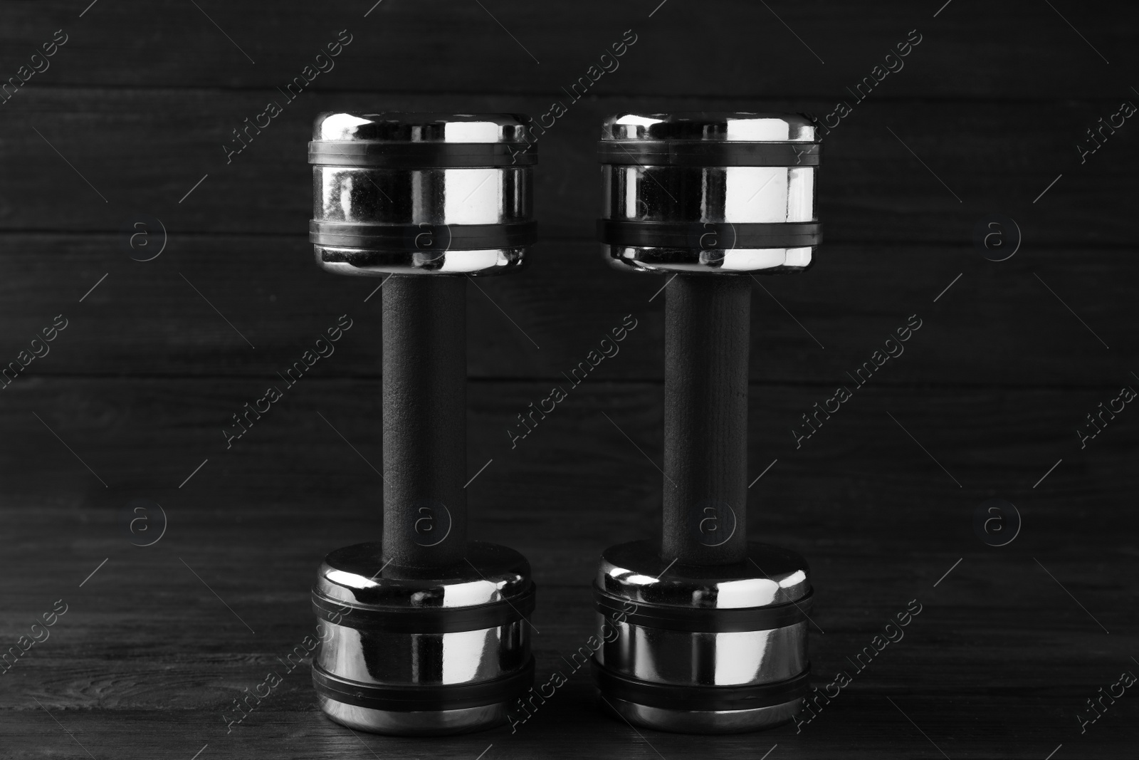 Photo of Two metal dumbbells on black wooden table