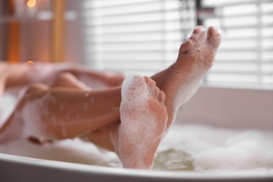 Photo of Woman taking bath in tub with foam indoors, closeup