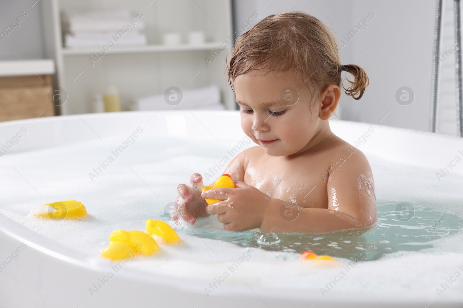 Photo of Cute little girl with rubber ducks in foamy bath at home