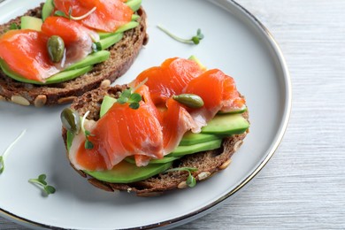 Delicious sandwiches with salmon, avocado and capers on white wooden table, closeup