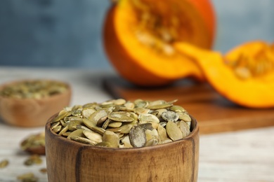 Photo of Bowl of raw pumpkin seeds on white table, closeup