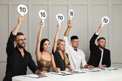 Photo of Panel of judges holding signs with highest score at table against light wall