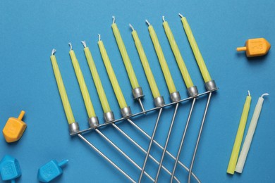 Photo of Hanukkah menorah with candles and dreidel on light blue background, flat lay
