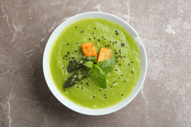 Delicious asparagus soup in bowl on grey marble table, top view