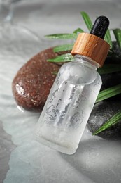 Photo of Bottle of face serum, spa stones and leaf on wet grey marble table, closeup