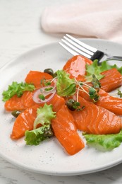 Salmon carpaccio with capers, lettuce, microgreens and onion on white wooden table, closeup