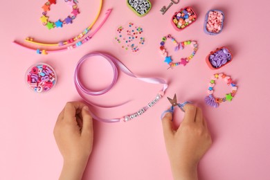 Photo of Child making beaded jewelry and different supplies on pink background, top view. Handmade accessories